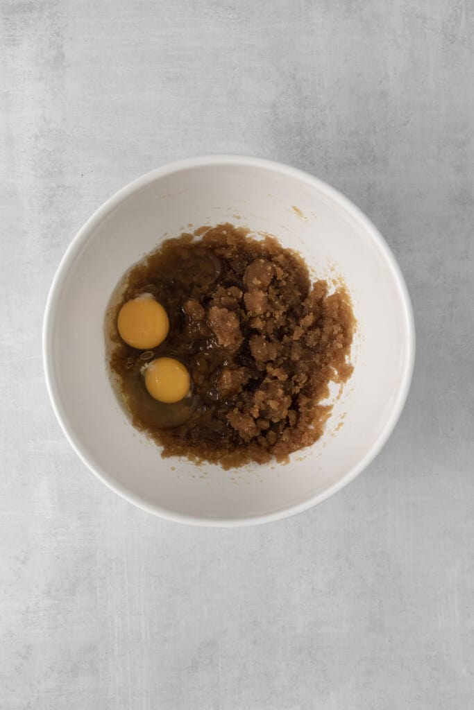 Top view of vegetable oil, brown sugar, eggs and vanilla extract in a mixing bowl.