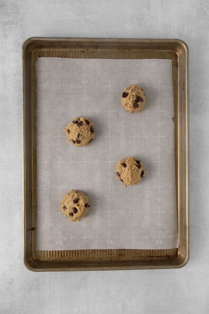 Baking sheet lined with parchment paper with 4 scoops of cookie dough on top.
