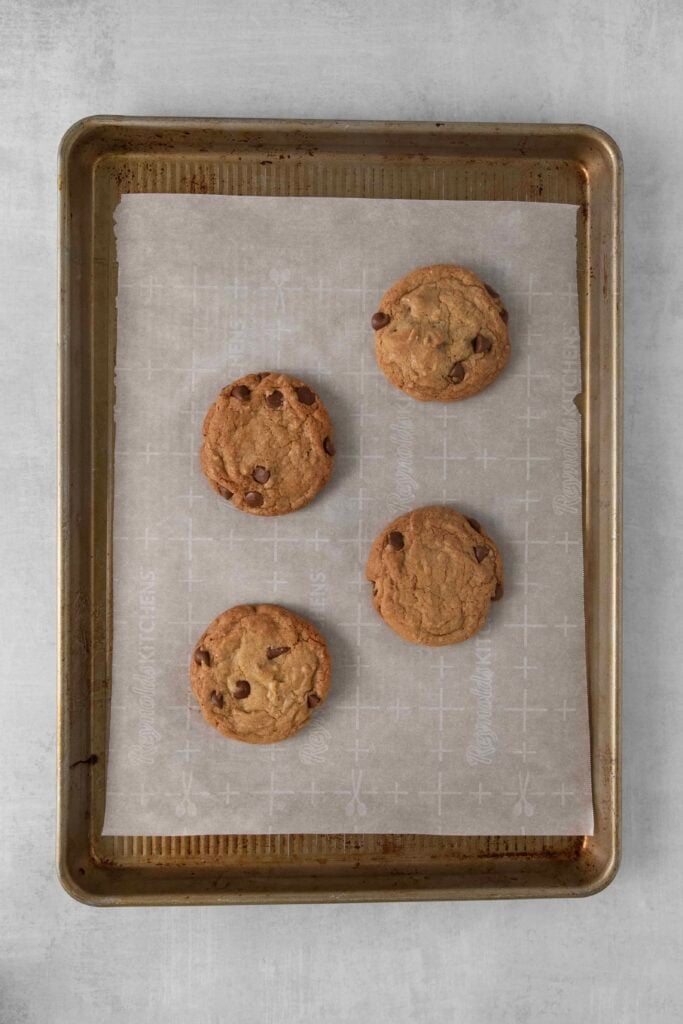 Baking sheet lined with parchment paper with 4 baked chocolate chip cookies.