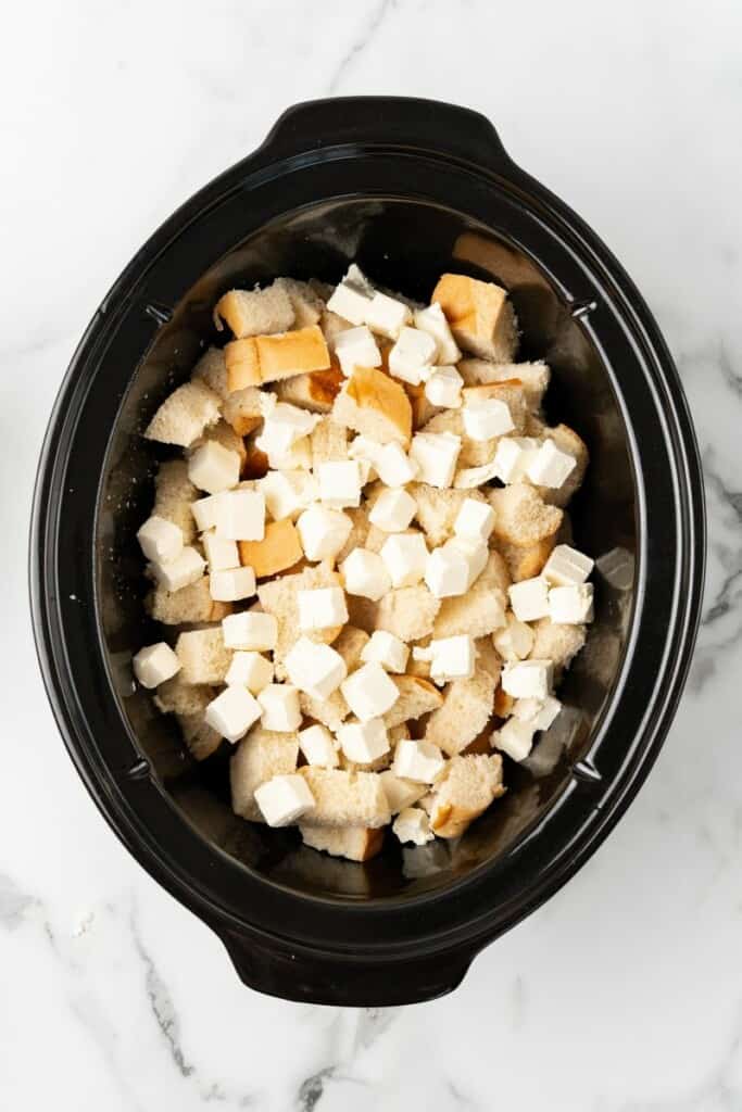 Overhead view of bread cubes and cream cheese in a crockpot.