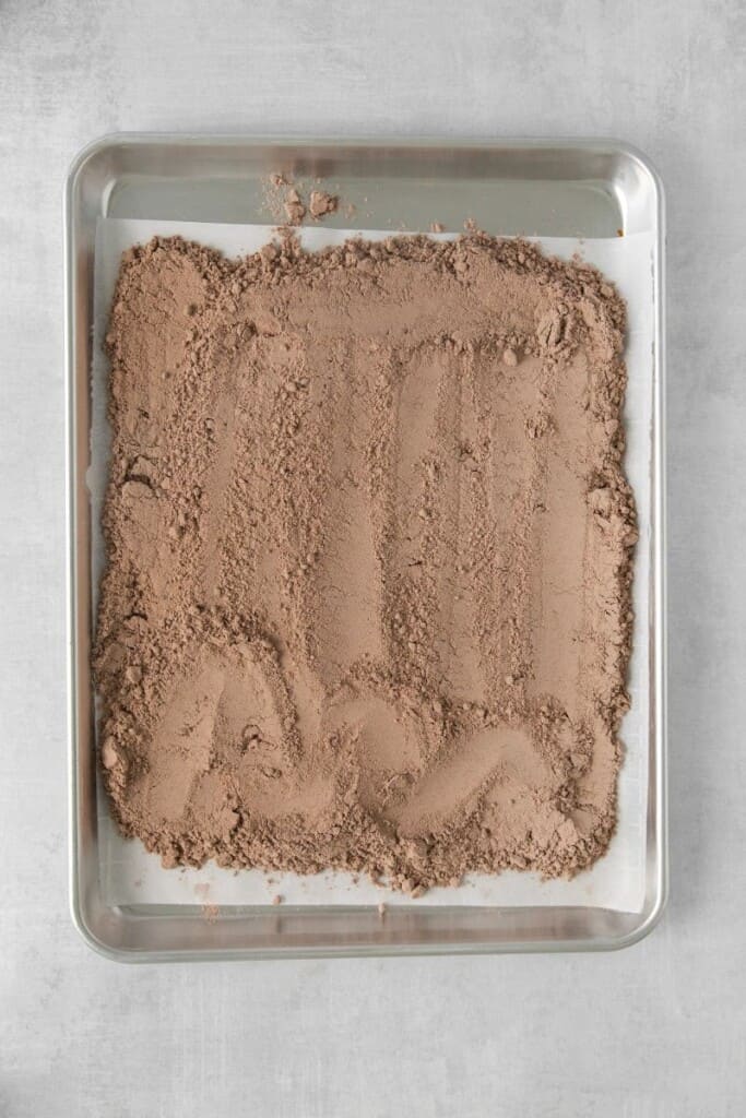 Brownie mix spread across the bottom of a baking pan lined with parchment paper.