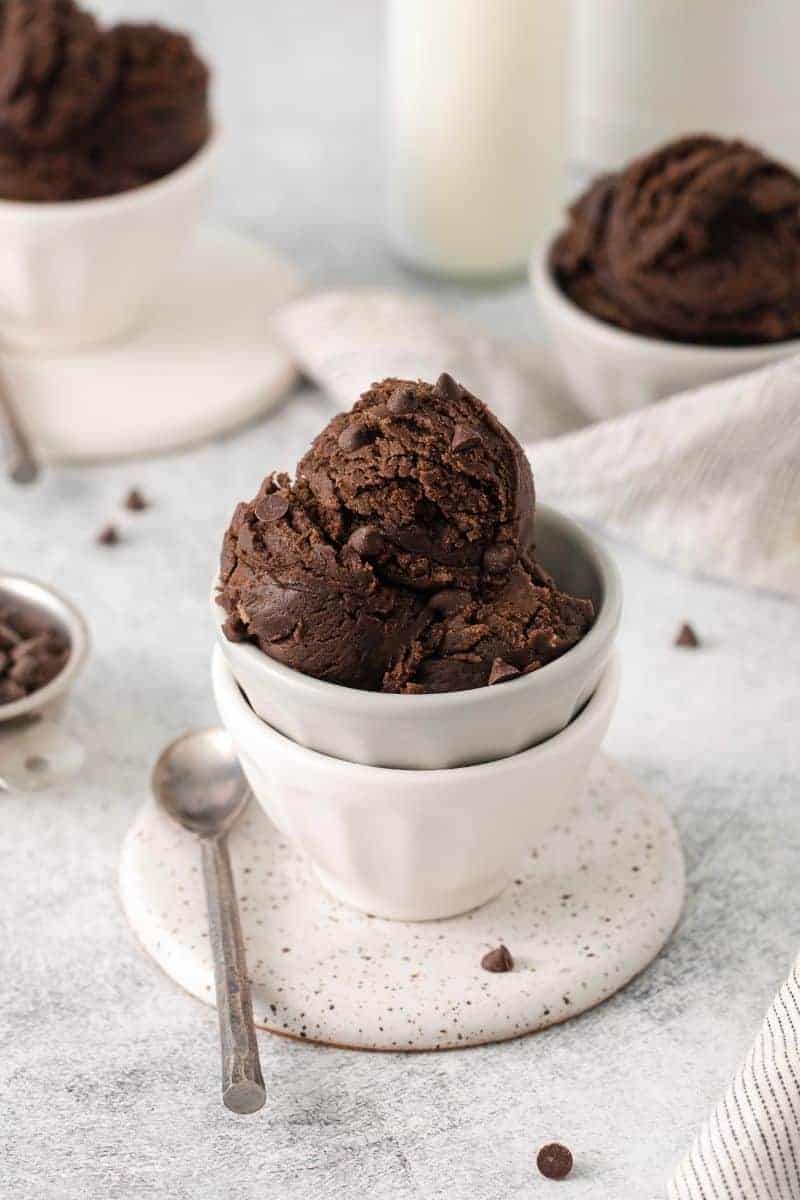 Edible brownie batter in a white bowl with a spoon on the side