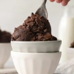 Scoops of edible brownie batter in stacked white bowls with a spoon on top.