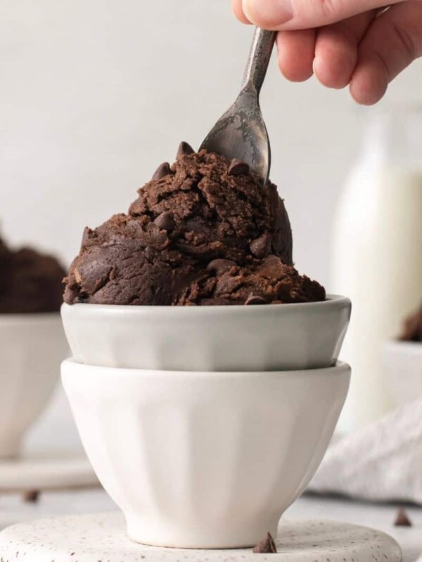 Scoops of edible brownie batter in stacked white bowls with a spoon on top.