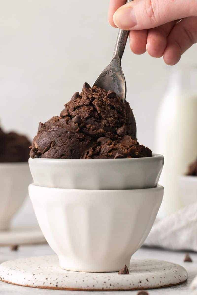 Scoops of edible brownie batter in stacked white bowls with a spoon on top.