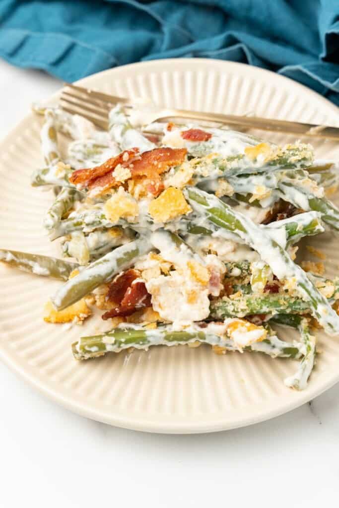 A serving of Green Bean Casserole with Cream Cheese on an off white plate.