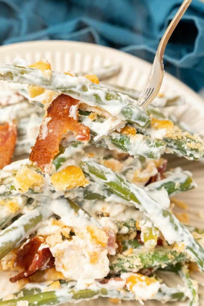Closeup view of a single serving of green bean casserole with cream cheese on an off white plate.