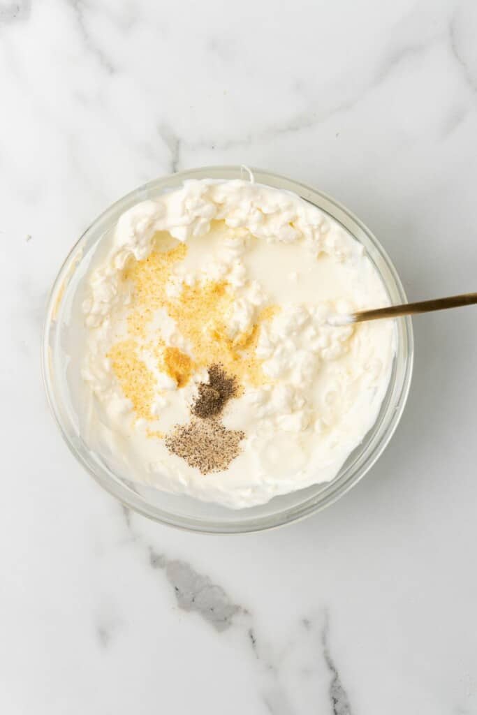 Cream cheese filling mixture in a clear bowl with a spoon.