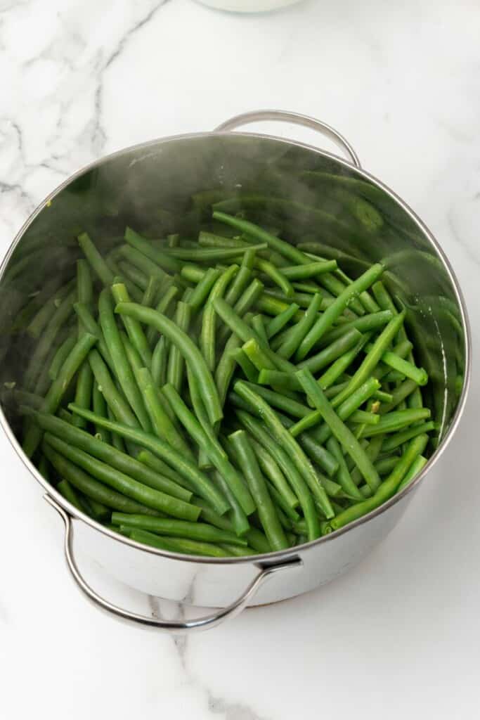 Overhead view of green beans in water, ready to cook in a silver pot.
