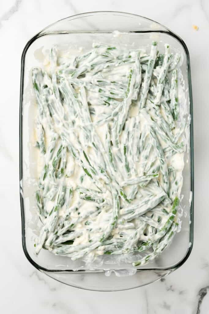 Green Beans and cream cheese mixture in a clear 9x13 baking dish.