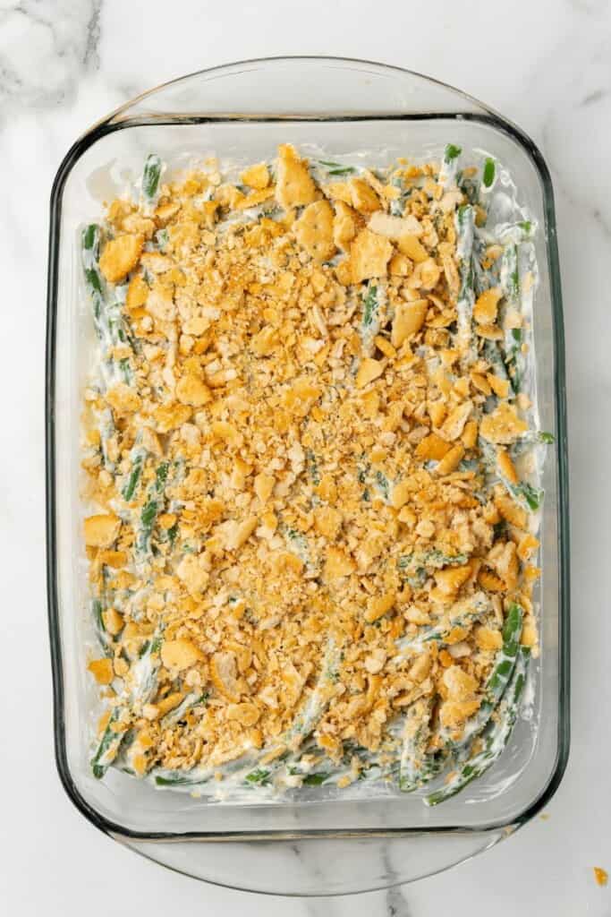 Crushed Ritz Crackers with melted butter sprinkled over the top of the green bean casserole in a clear 9x13 baking dish.
