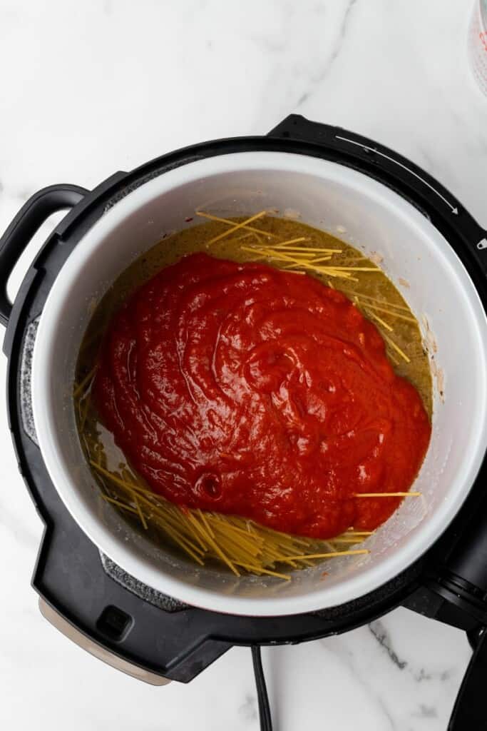 Overhead view of pasta and spaghetti sauce added to the Ninja Foodi.