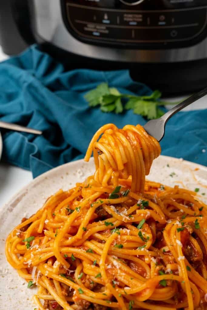 A fork holding a bite of spaghetti on an off white plate.