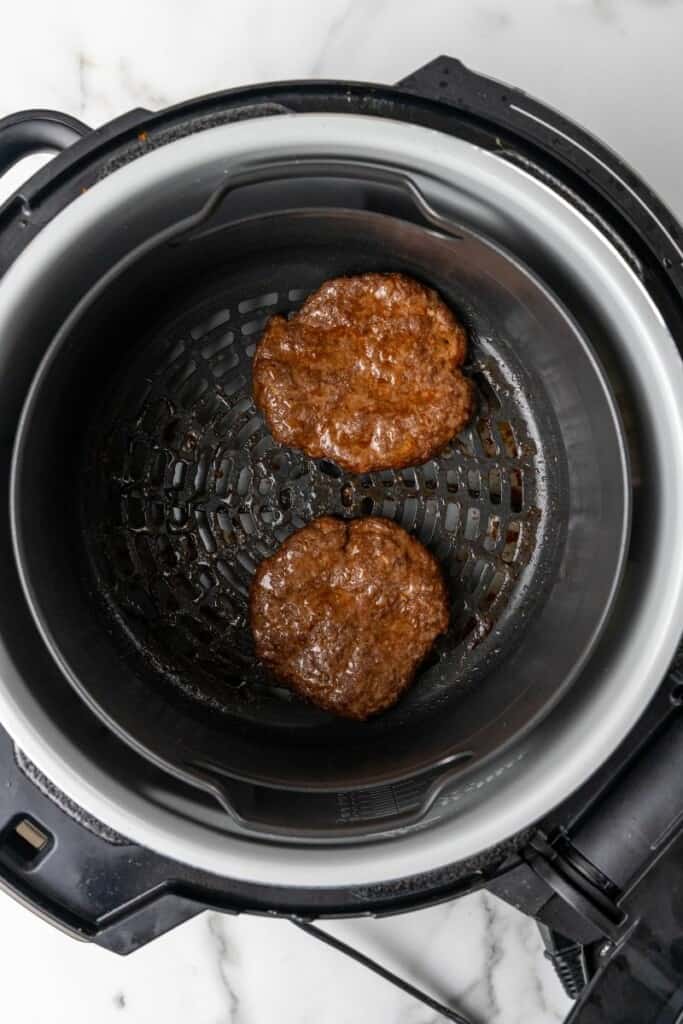 Two cooked hamburger patties resting in the bottom of a Ninja Foodi.