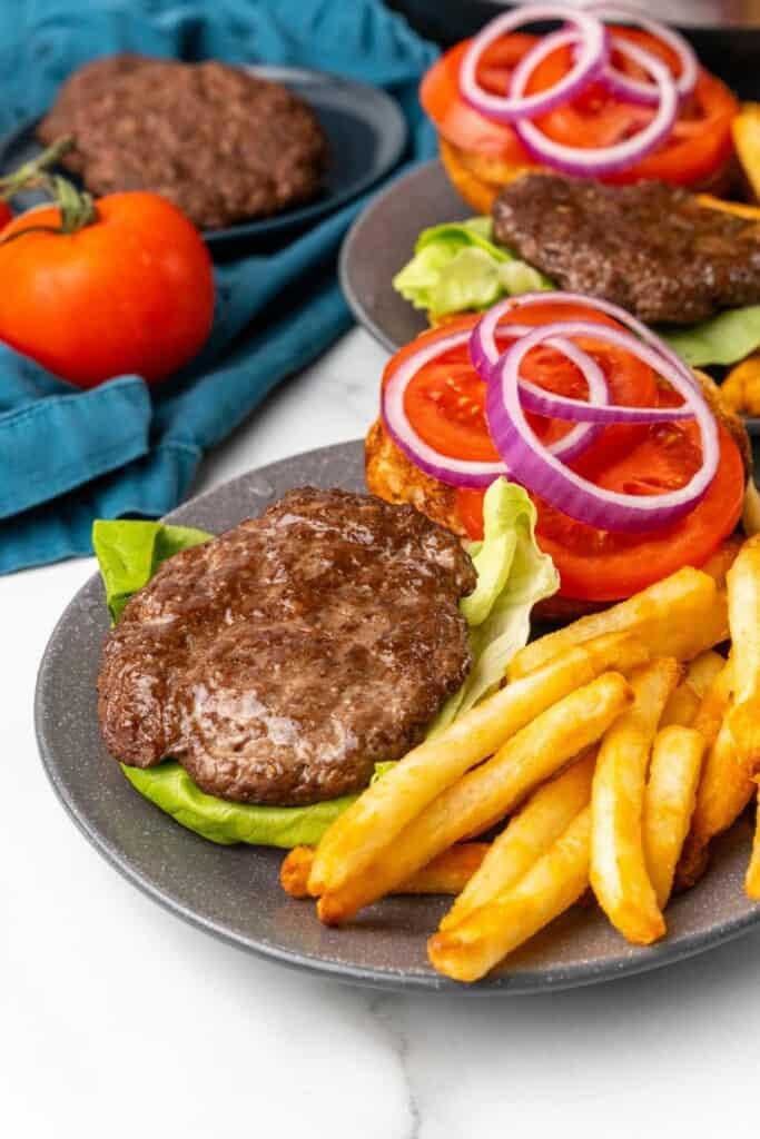 Open face hamburger patty and toppings on a gray plate with french fries.