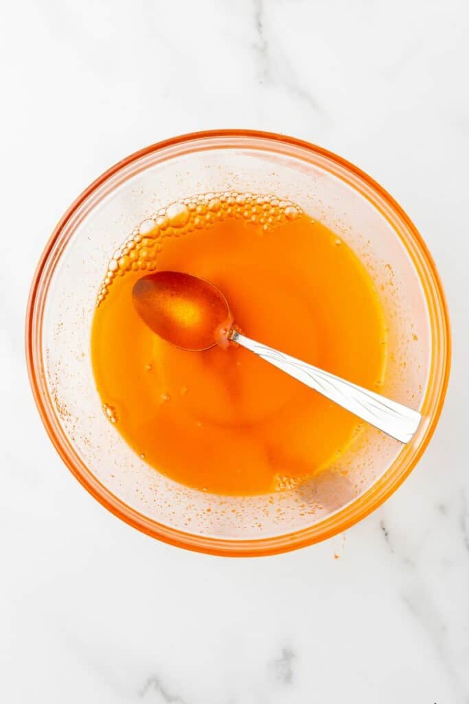 Overhead view of Jello powder mixed with boiling water in a clear bowl with a spoon to stir.