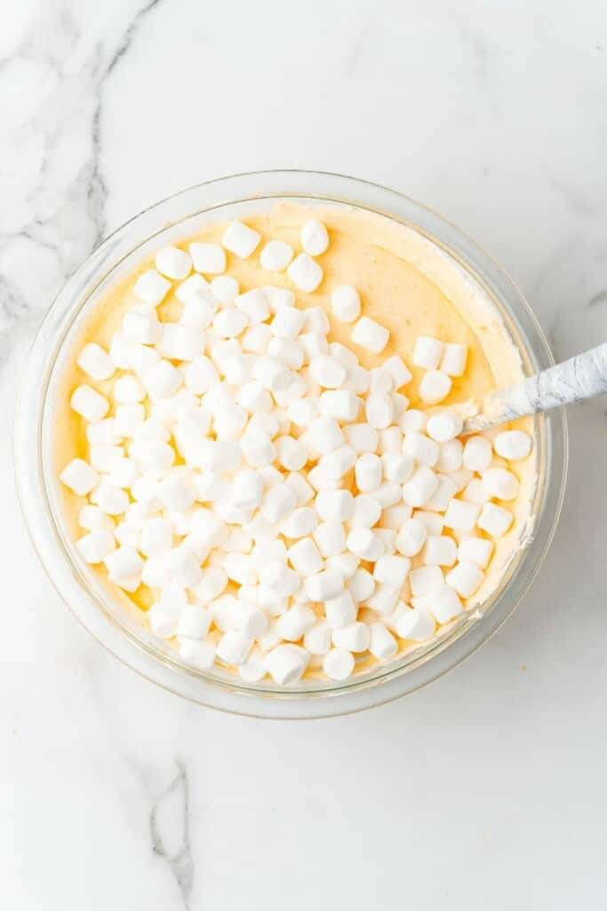 Small marshmallows on top of Orange Dreamsicle Salad in a clear bowl with a spoon.
