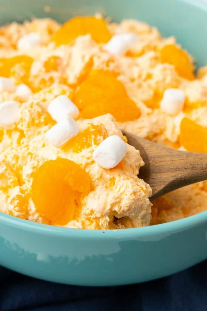 Close up view of orange dreamsicle salad in a blue bowl with a spoon.