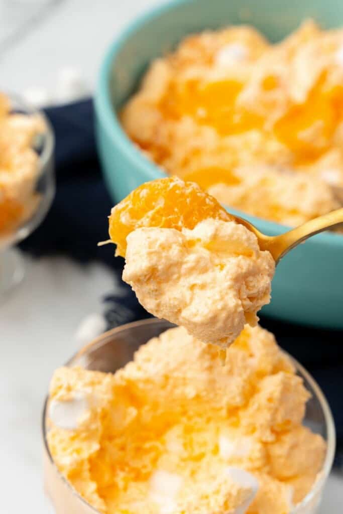 Spoonful of orange dreamsicle salad. Small clear bowl of salad and larger blue bowl of salad in background.