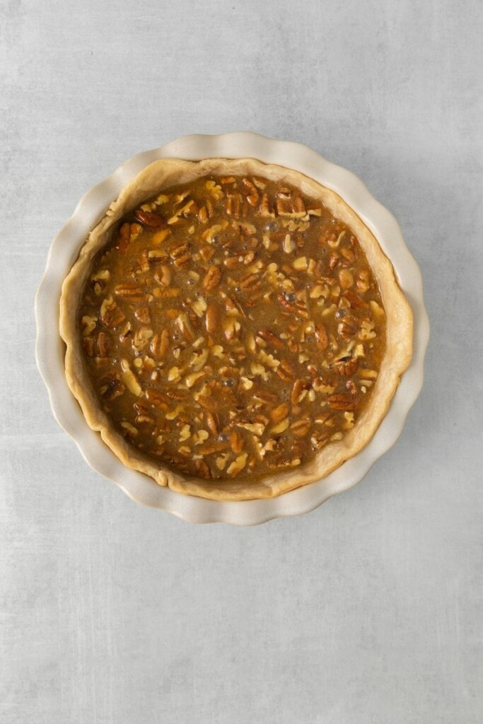 Pecan pie filling poured into pie crust in a round baking pan.