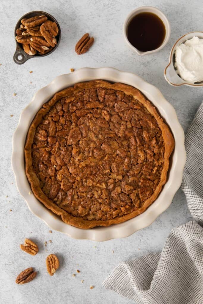 Baked pecan pie in a round baking dish with pecans sprinkled around.