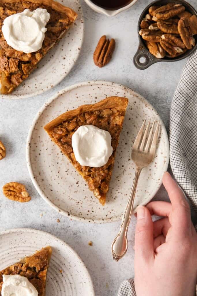Slices of pecan pie without corn syrup topped with whipped cream on off white plates.