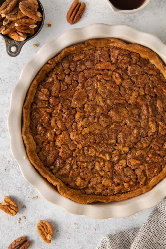 Baked pecan pie in a round baking dish with pecans sprinkled in the background.