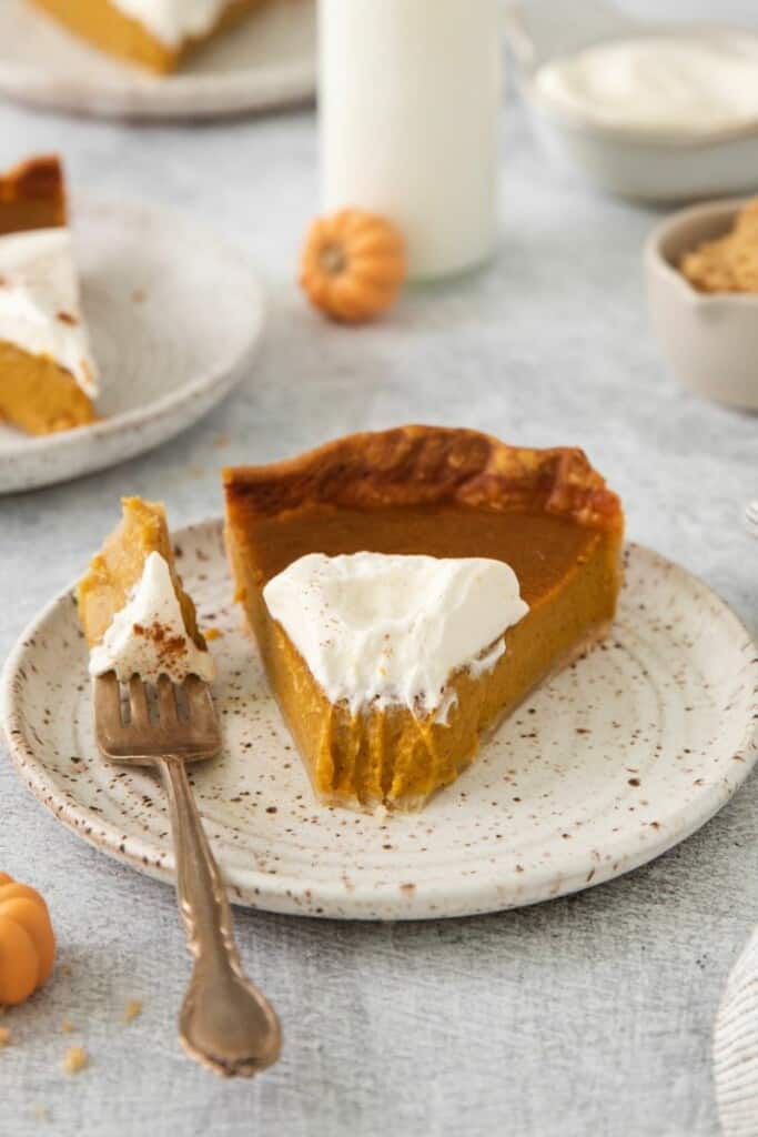 Slice of pumpkin pie with whipped cream. One bite resting on a fork.