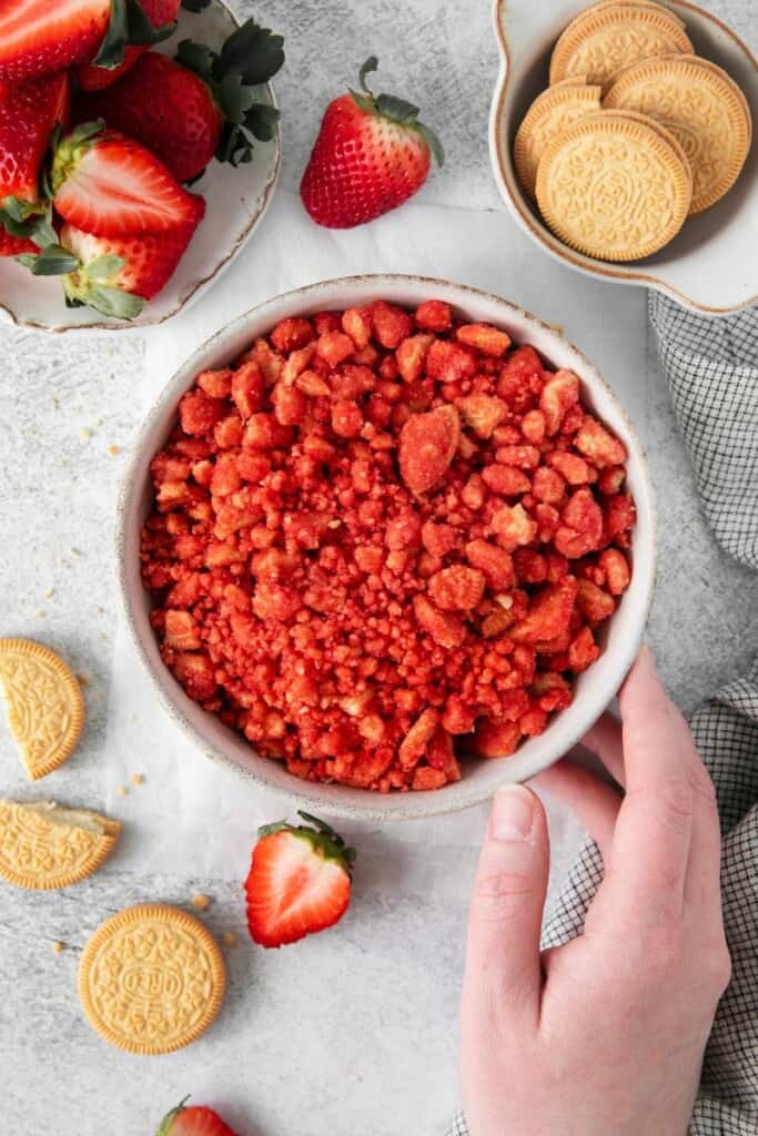 Overhead view of Strawberry crunch mix in a white bowl witih oreos and strawberries in the background.