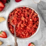 Overhead view of strawberry crunch in a white bowl with a spoon. Oreos and strawberries in background.