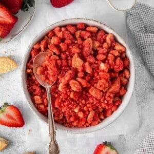Overhead view of strawberry crunch in a white bowl with a spoon. Oreos and strawberries in background.