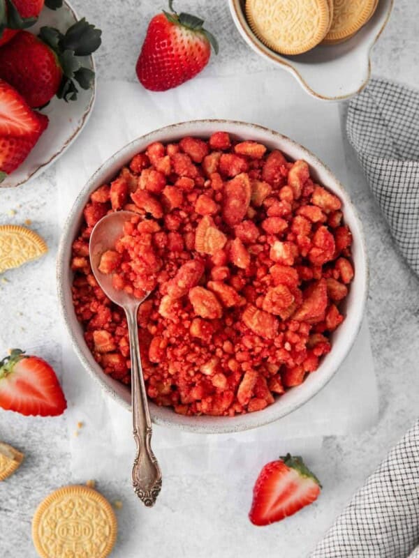 Overhead view of strawberry crunch in a white bowl with a spoon. Oreos and strawberries in background.