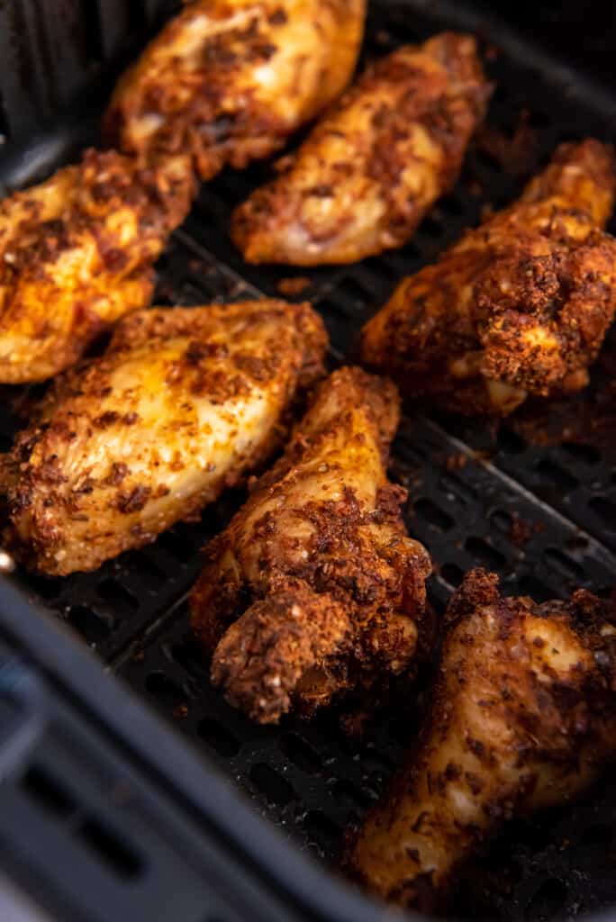 Overhead view of cooked chicken wings in an air fryer basket.