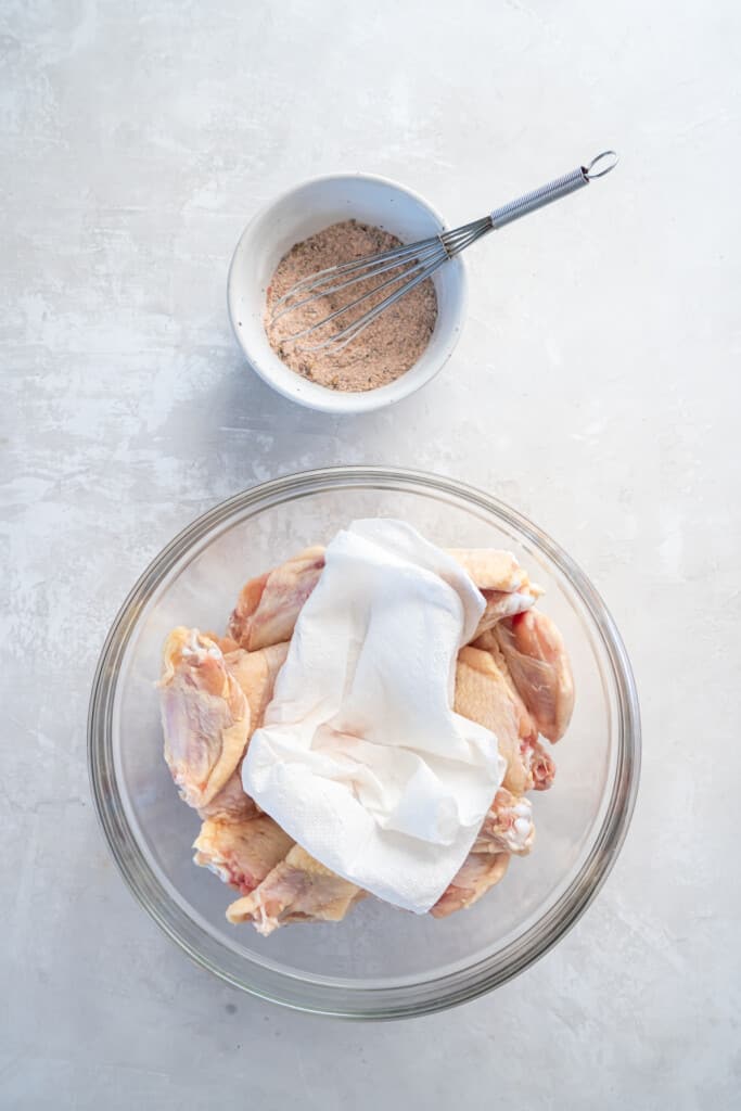 Overhead view of chicken wings in a clear bowl with a paper towel to remove moisture.