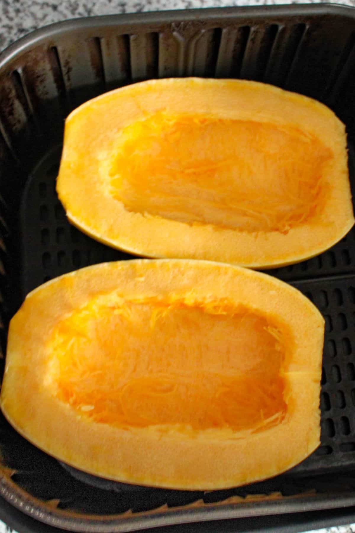Halved spaghetti squash in an air fryer basket.
