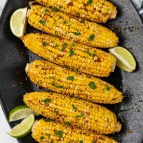Plated cajun corn on the cob recipe on a black serving dish with lime wedges.