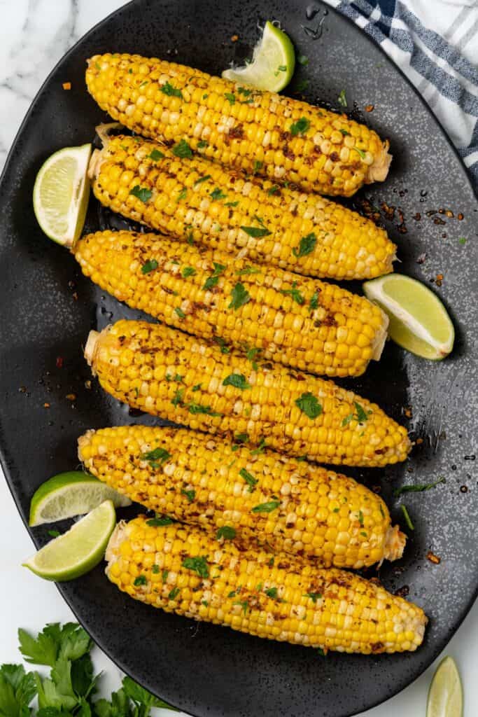 Plated cajun corn on the cob recipe on a black serving dish with lime wedges.