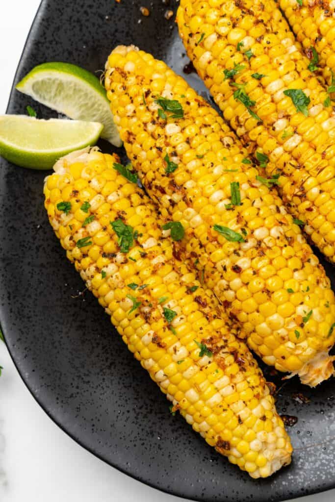 Close up of cajun corn on the cob on a black serving plate with lime wedges.
