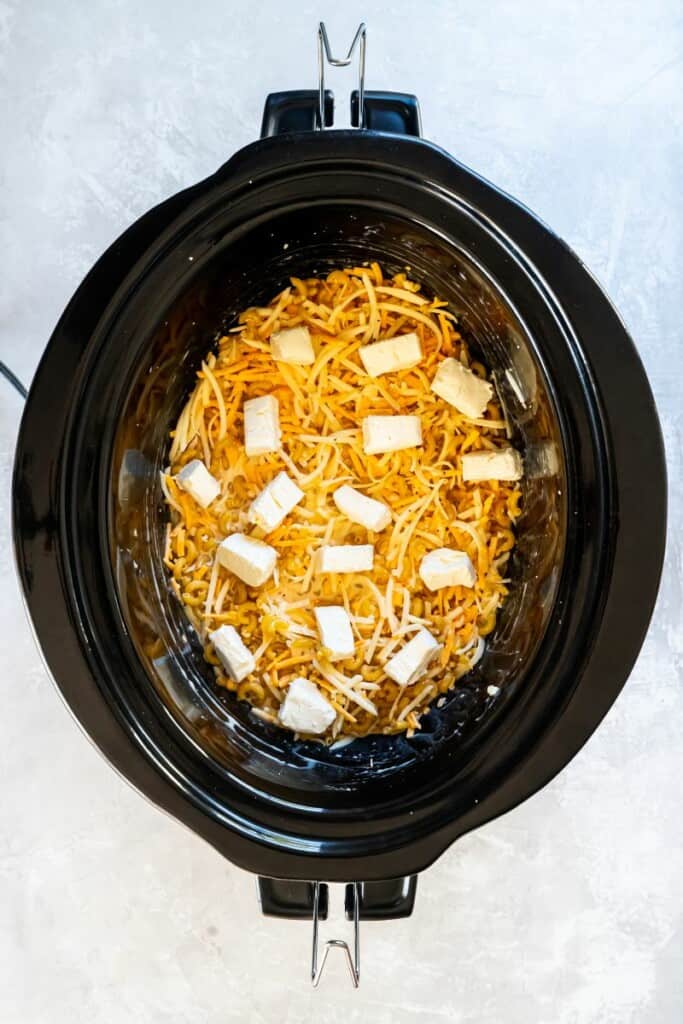 Ingredients for macaroni and cheese added to a black slow cooker, ready to cook.