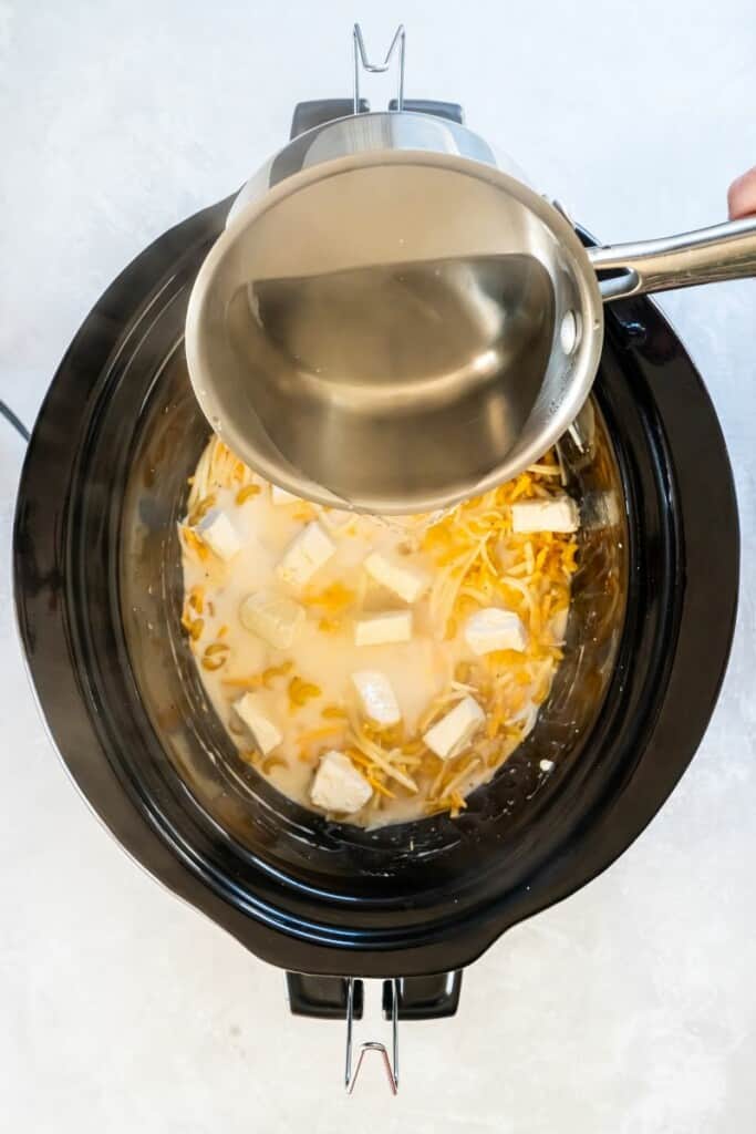 Adding water to macaroni and cheese ingredients in a black crock.