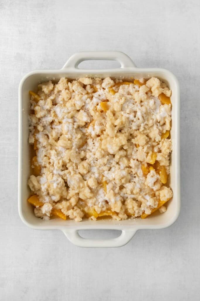 Flour, sugar and butter combined and sprinkled over peaches in a square white baking dish.