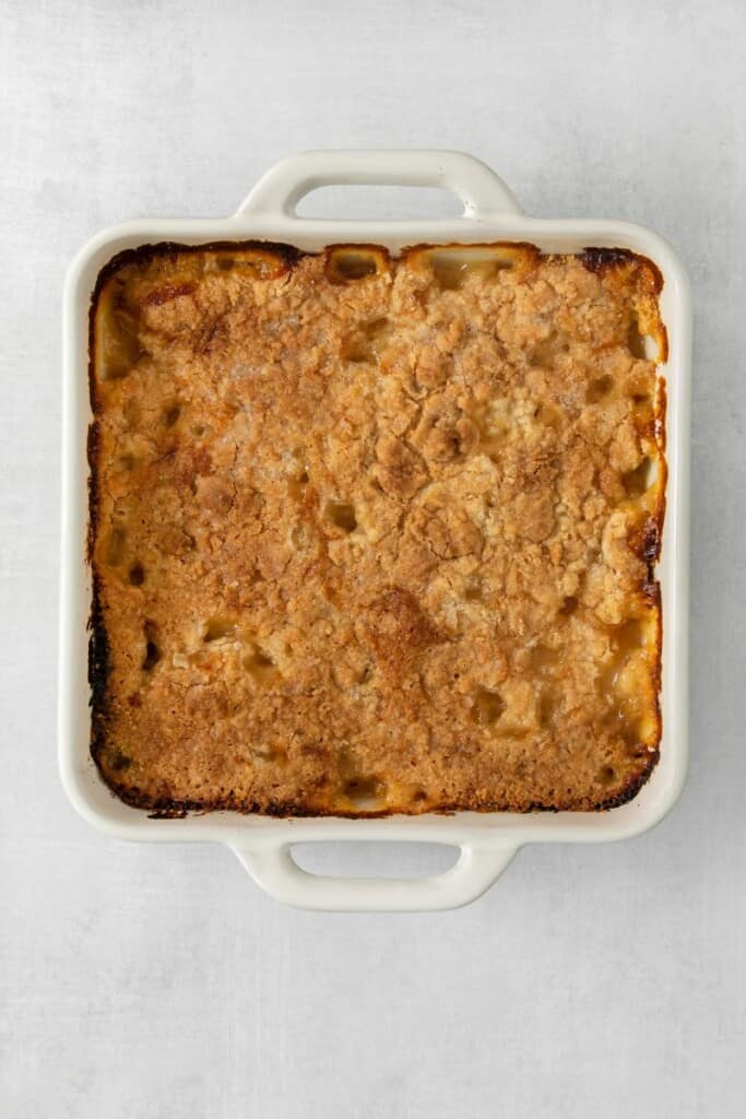 Baked peach cobbler in a square white baking dish.