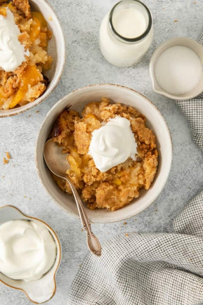A single serving of peach cobbler in a bowl topped with whipped cream.