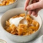 Peach cobbler in a bowl with a spoon lifting a bite.