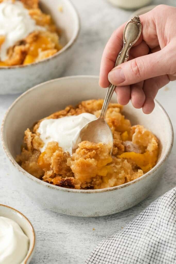 Peach cobbler in a bowl with a spoon lifting a bite.