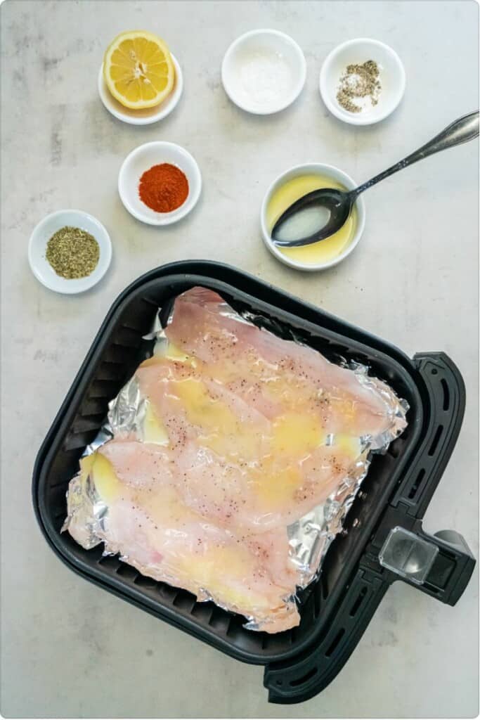 Seasoned flounder topped with butter, lemon juice, and garlic in a black air fryer basket.