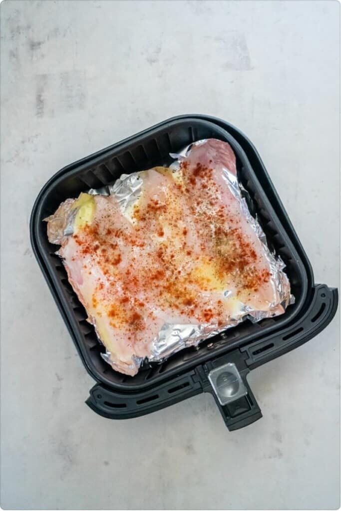 Paprika and Italian Seasoning on Flounder in a black air fryer basket.