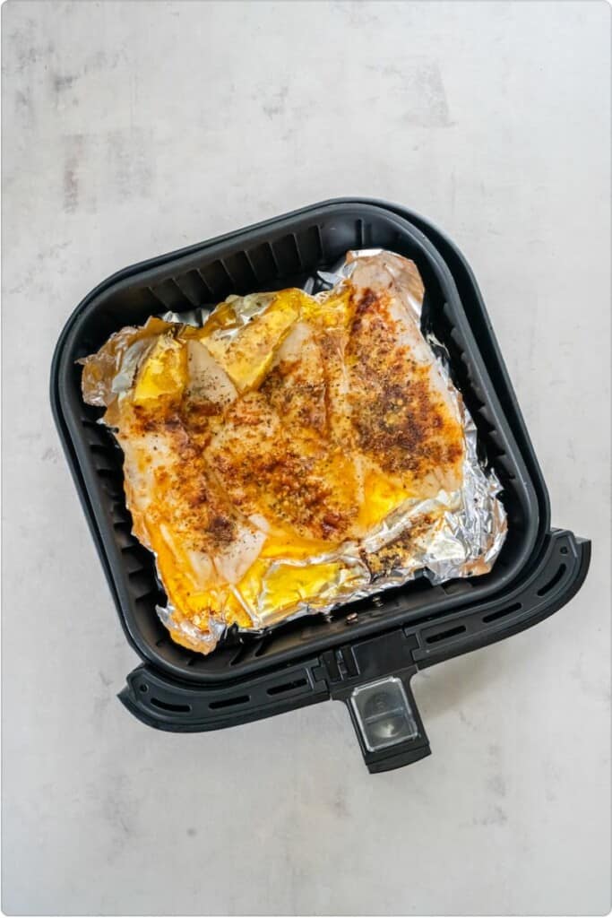 Seasoned flounder fully cooked resting in a black air fryer basket.