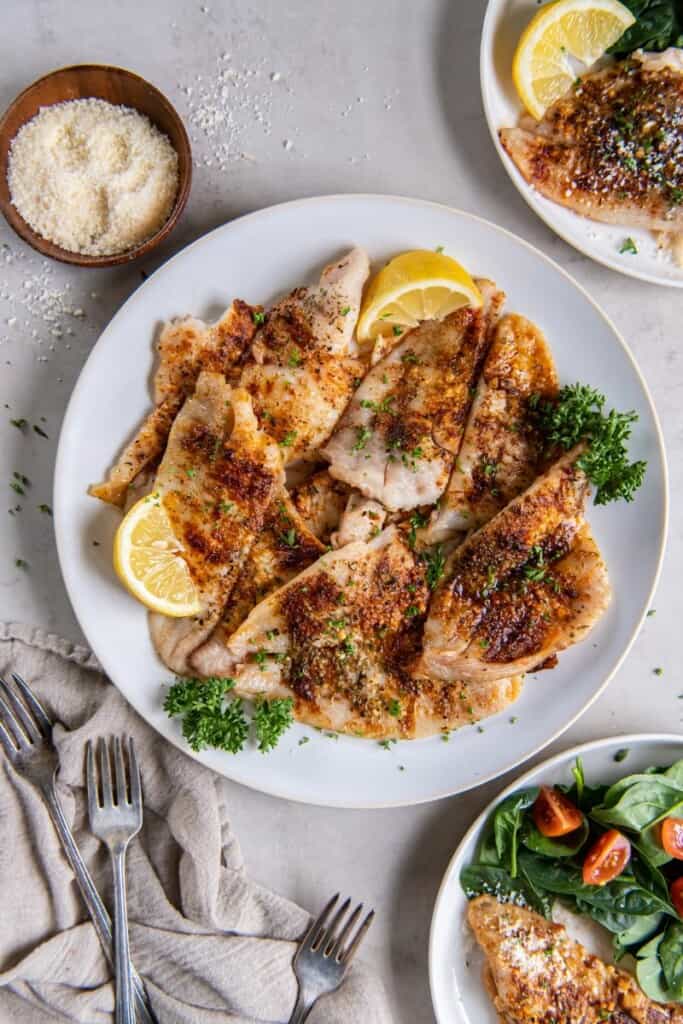 A white plate with fully cooked flounder and lemon wedges.