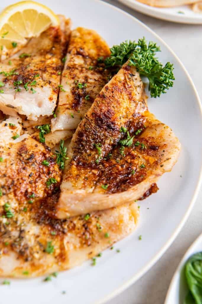 A closeup view of an air fried piece of flounder on a white plate.